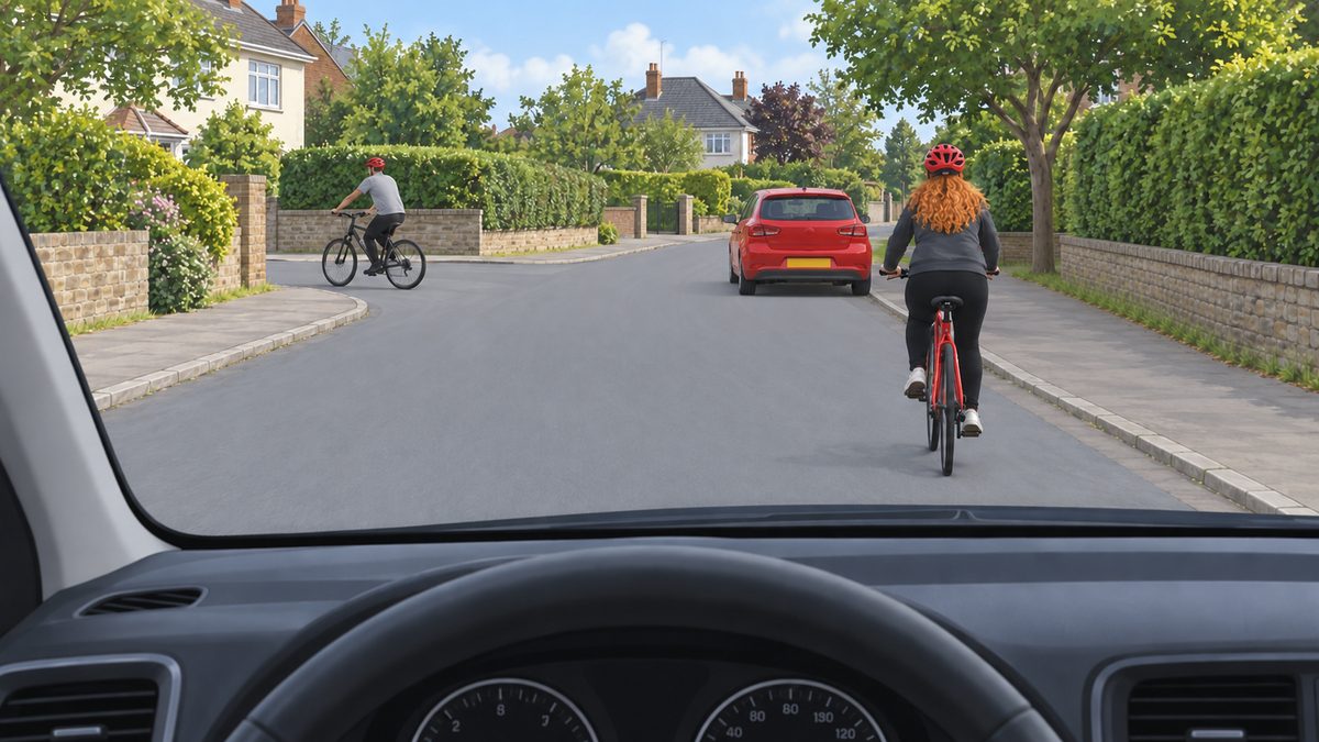 Two cyclists on a residential street with a parked red car ahead.