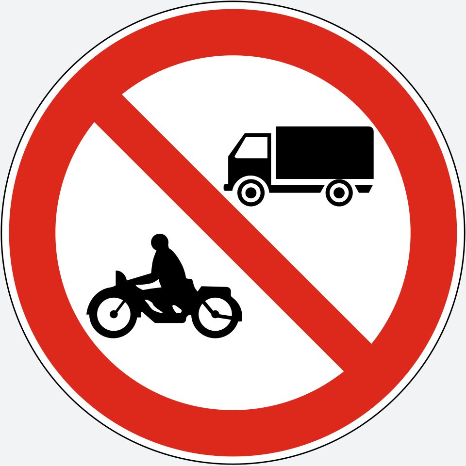 White circle with a red border and a red diagonal stripe from upper left to lower right; a black truck at upper right and a black motorcycle with rider at lower left, both facing left.
