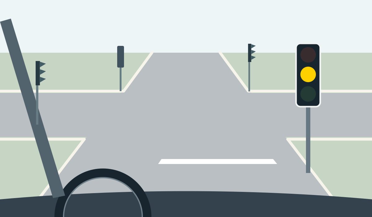 Driver view of an empty four-way junction and stop line. The facing signal has its amber lamp lit and its red and green lamps dark.