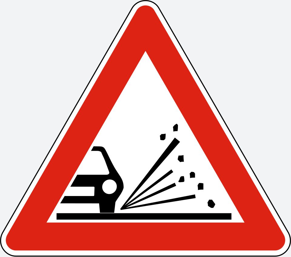 Red-bordered upright triangle; car wheel and small stones flying diagonally upward to the right.