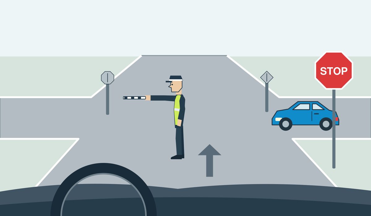 Driver view of a junction, a controller in left-facing profile with the right arm extended forward and the left arm down, a blue car approaching from the right, and a STOP sign.